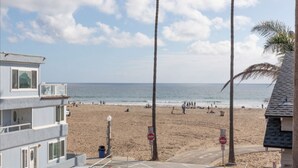 Vista de la playa con un área de estacionamiento, un edificio con balcón y cielo despejado.