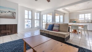 Amplia sala de estar con sofá, mesa de centro y mesa de comedor. Cuenta con ventilador de techo y un gran ventanal que proporciona luz natural.