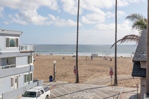 A beach view with a parking area, a building with a balcony, and a clear sky.