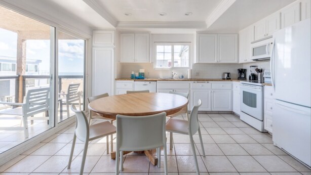 Una cocina moderna con armarios blancos, una mesa de comedor de madera y un amplio ventanal con vistas a un balcón.