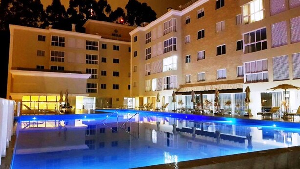 A hotel with a swimming pool, multiple floors, and outdoor seating areas. - Spend your holidays at a club. (Nações)