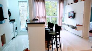 A modern kitchen with a washing machine, a dining area with chairs, a TV, and a large window with curtains. - Spend your holidays at a club. (Nações)
