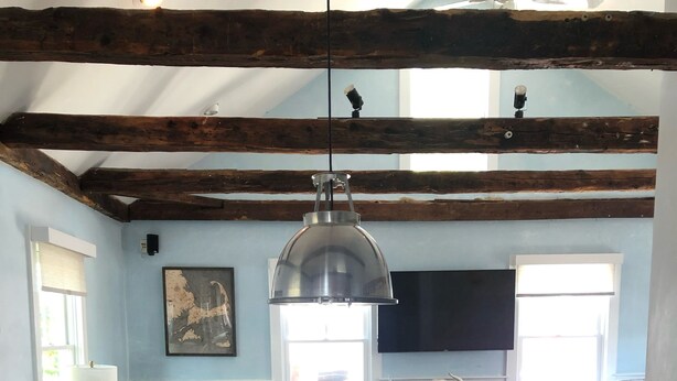 A rustic dining table with six chairs, a bottle of wine, and wine glasses. A wooden ceiling with exposed beams and a hanging light fixture are visible. - Charming 2br/2ba - steps 2 beach and all Ptown has to offer!  (Provincetown)