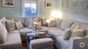 A living room with a sectional sofa, a coffee table, and a world map on the wall. - Charming 2br/2ba - steps 2 beach and all Ptown has to offer!  (Provincetown)