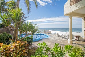 A pool area with lounge chairs and a view of the sea.