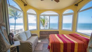 Una habitació amb un llit, un sofà, una taula petita i grans finestres amb vista a l'oceà.