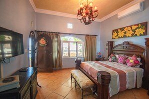 A bedroom with a bed, bench, TV, dresser, and a window with curtains.
