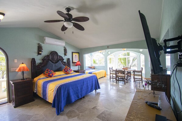 A bedroom with two beds, a ceiling fan, an air conditioner, a TV, and a dining area with chairs and a table.