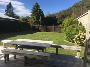Relax on the patio with a wooden picnic table and benches, surrounded by lush greenery and a stone wall.
