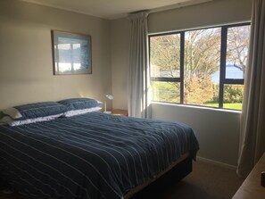 Relax in this serene bedroom with a large bed, bedside table, and a beautiful view of the surrounding trees and water.