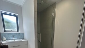 A modern bathroom with a glass shower enclosure, a sink with a mirror, and a window above the sink. - Stunning beach front bach (Kinloch)