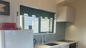 A compact kitchen with white cabinets, a black dishwasher, a sink, and a window with a lattice design. - Stunning beach front bach (Kinloch)
