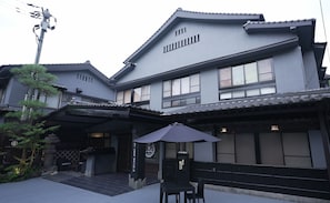 Een traditioneel Japans gebouw met een overdekte entree, een stenen lantaarn en een klein terras.