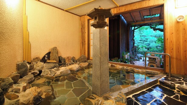 A traditional Japanese onsen with a stone bath, wooden interior, and a view of a garden through the entrance. - Furuyu Onsen Kakureisen (Saga)