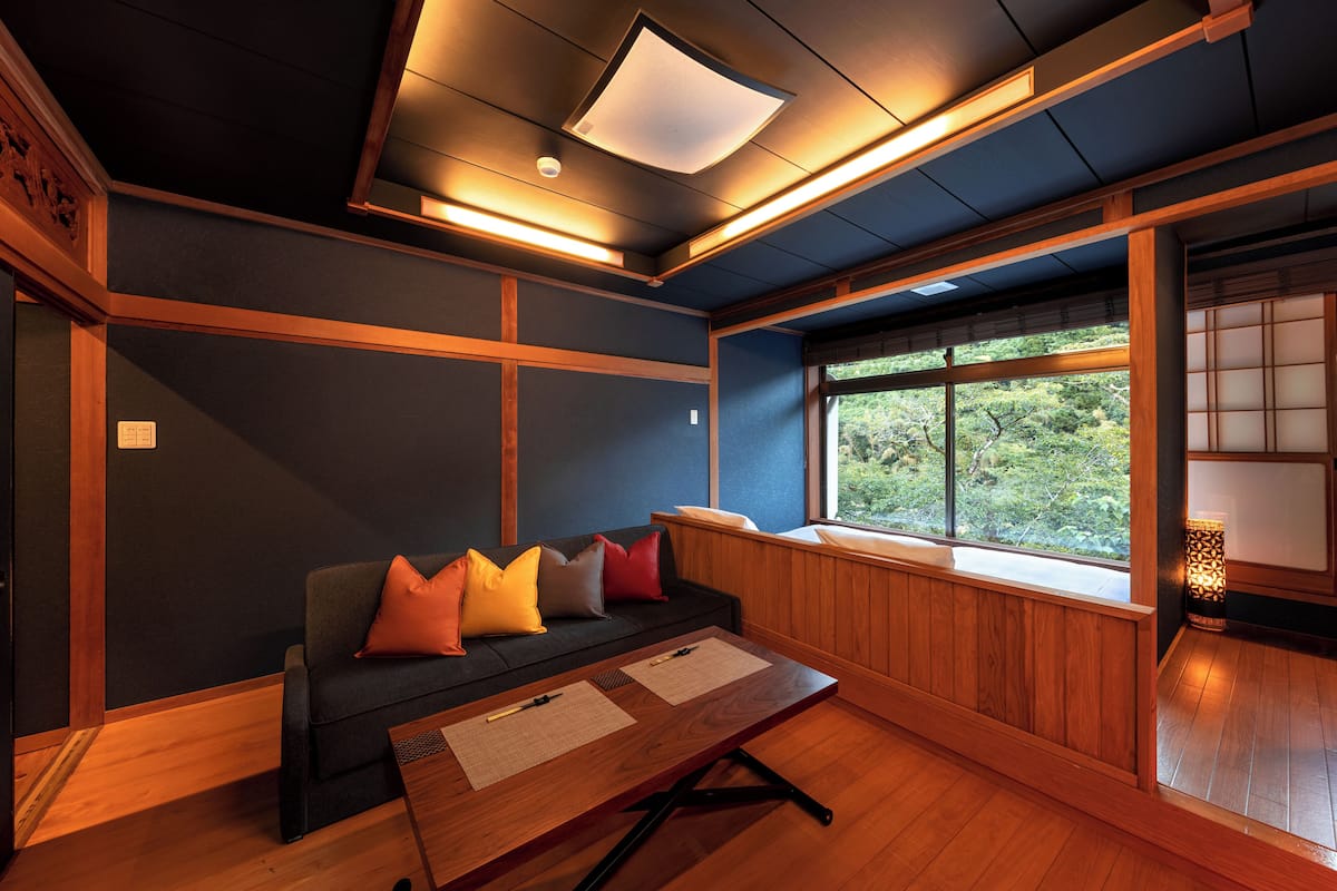 Een traditionele Japanse kamer met tatami vloerbedekking, een lage houten tafel en een donkergroene bank met kussens.
