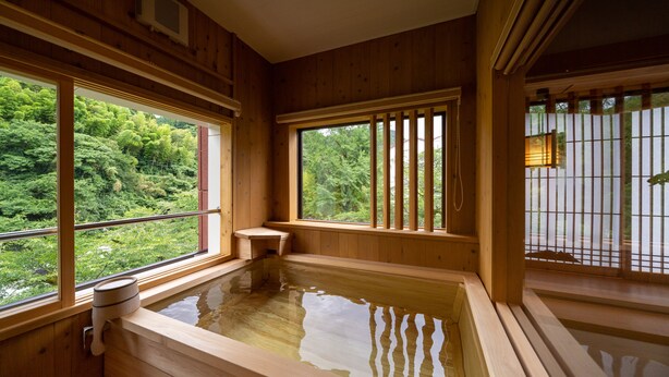 Een houten kamer met een warmwaterbad, grote ramen en uitzicht op weelderige begroeiing.