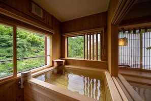 Une pièce en bois avec un bain à remous alimenté par une source d’eau chaude, de grandes fenêtres et une vue sur une végétation luxuriante.