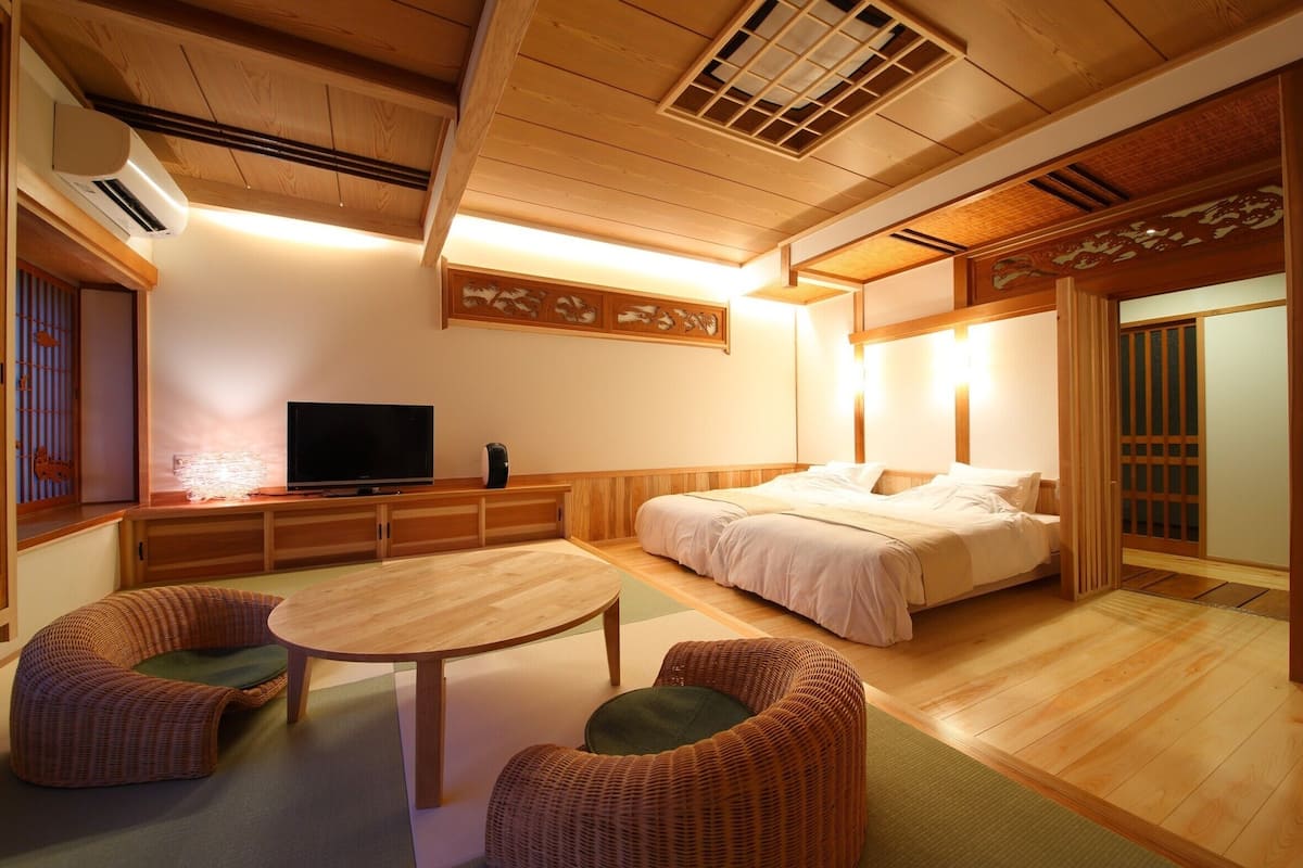 Een traditionele Japanse kamer met tatami vloerbedekking, een bed, een televisie en een eettafel.