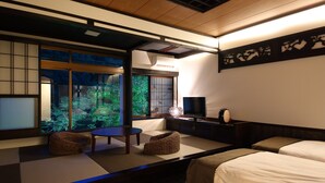 Een traditionele Japanse kamer met tatami vloeren, een televisie en uitzicht op groen buiten.
