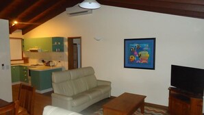 A living room with a sofa, a coffee table, a TV, and a kitchen area with a sink and cabinets.