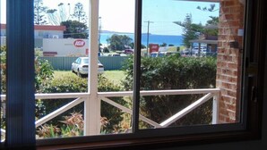 A view from a window with a balcony, overlooking a parking area with cars and a building with 'IGA' signage.