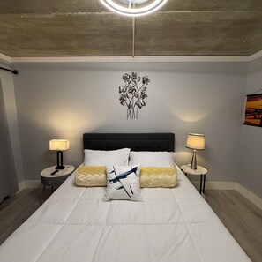 Une chambre d’hôtel comprenant un lit, deux tables de chevet, un luminaire fixé au mur et un élément décoratif mural.