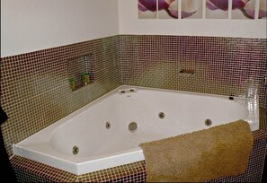 Ein Badezimmer mit einer großen Badewanne, gefliesten Wänden und einem Handtuch auf dem Boden.