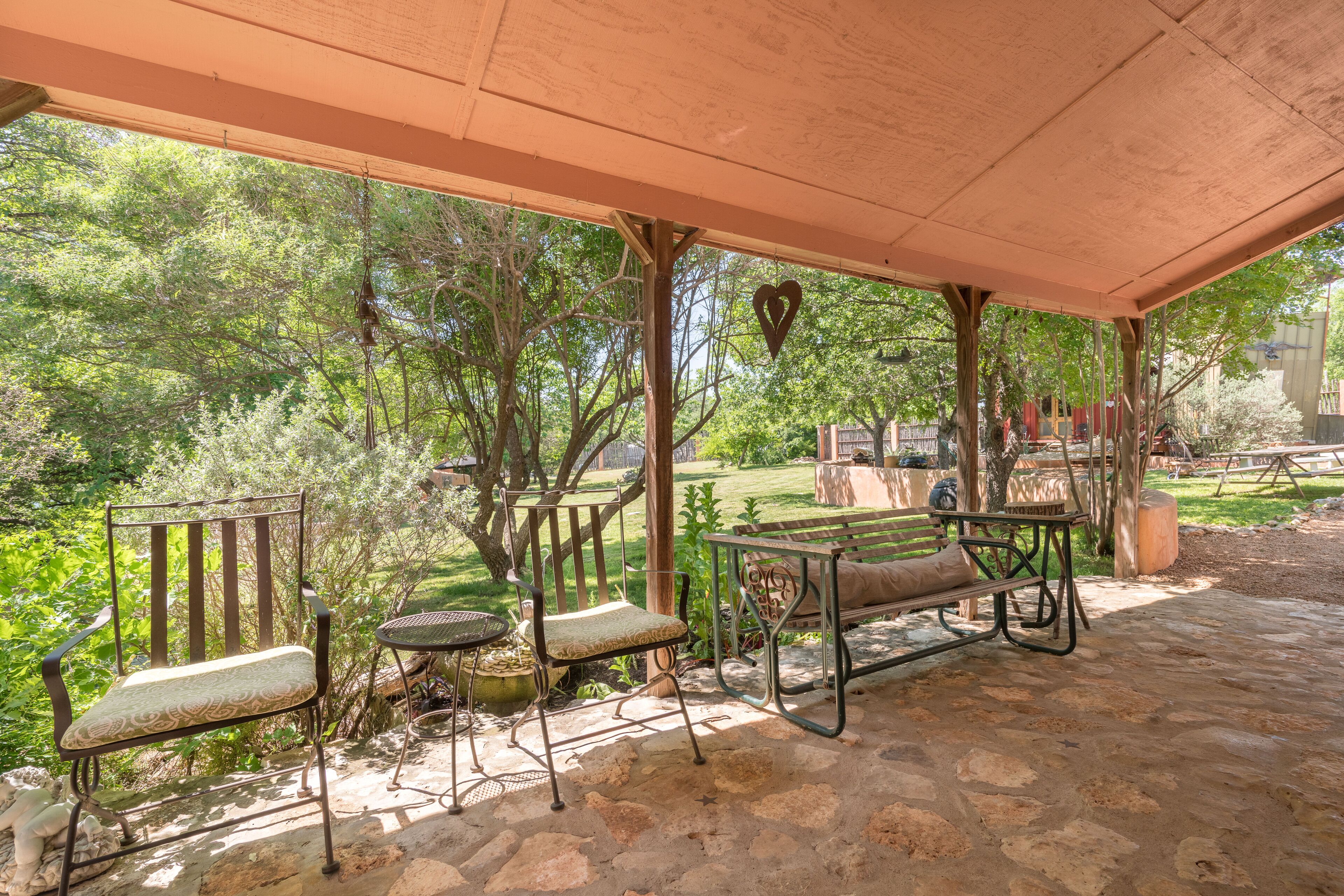 An outdoor patio with stone flooring, metal furniture, and a view of a garden and trees.