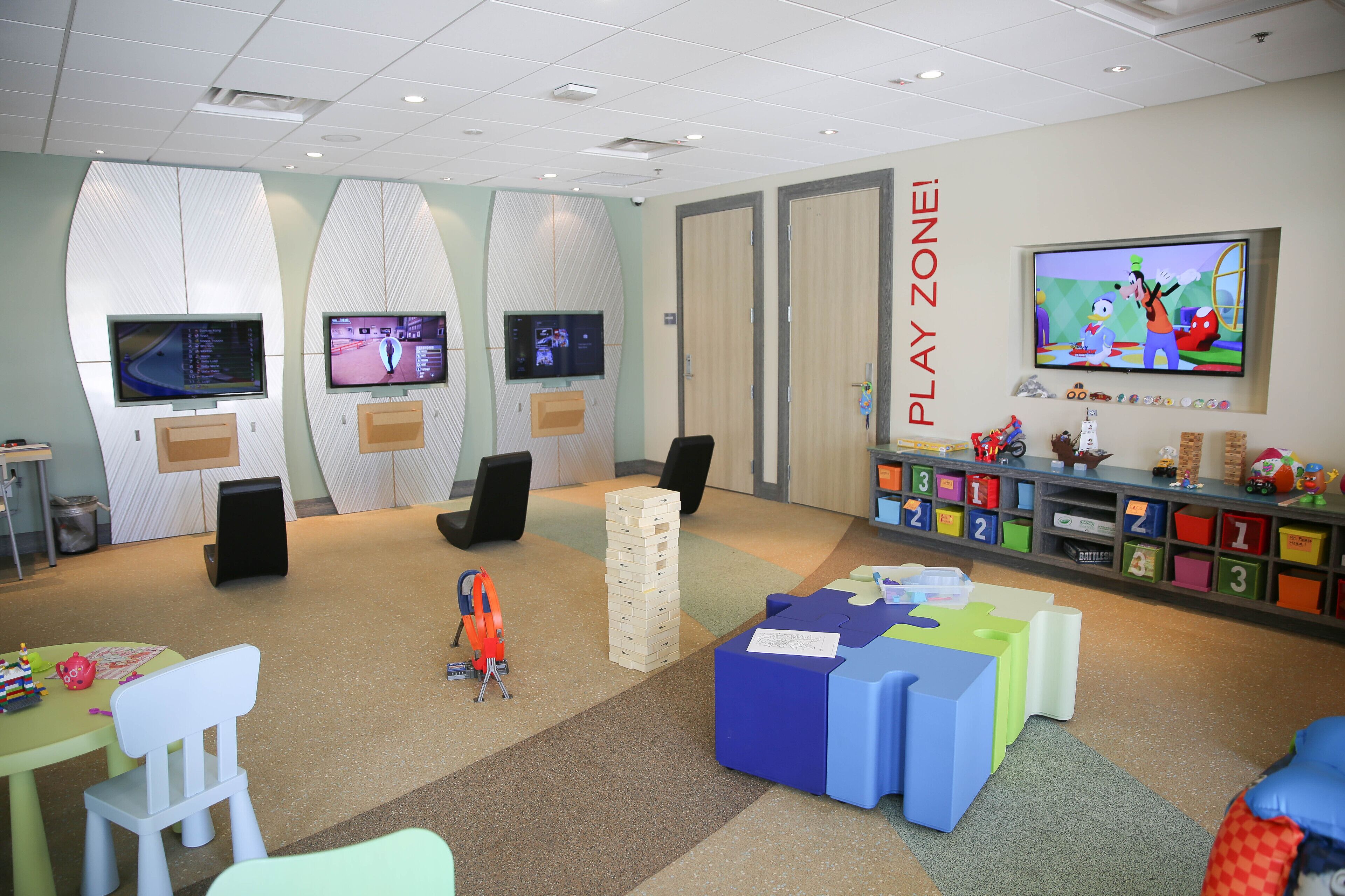 A play zone with multiple TVs, a play area with toys, and a colorful storage unit with numbered boxes.