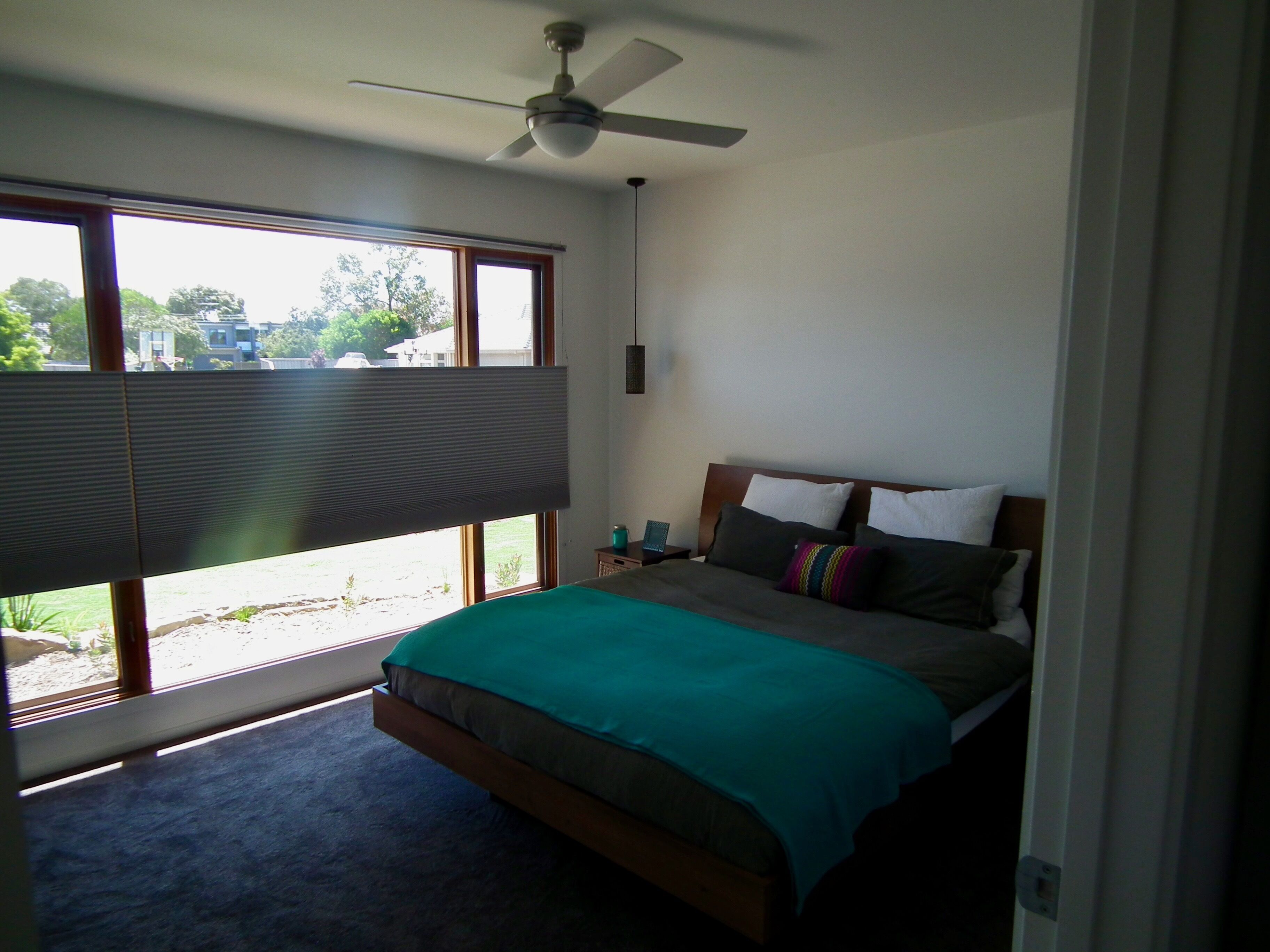 A bedroom with a bed, a ceiling fan, a window with blinds, and a view of the outside.