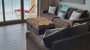 Una sala de estar con un sofá, un reposapiés y vista a la playa a través de un cerramiento de vidrio corredero.