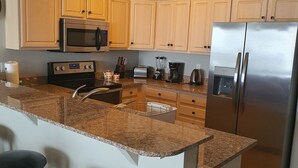 Una cocina con encimeras de granito, electrodomésticos de acero inoxidable, armarios de madera y una isla central con taburetes de bar.