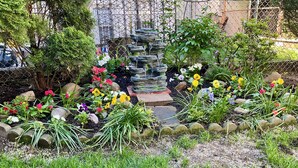 Un jardí amb una font de pedra, flors de colors i una tanca metàl·lica.