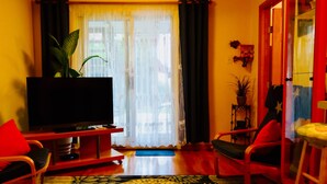 A living room with a flat-screen TV, a sofa, a chair, a small table, and a potted plant.