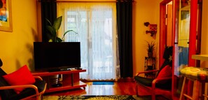 Una sala de estar con una televisión de pantalla plana, un sofá, una silla, una mesita y una planta en maceta.