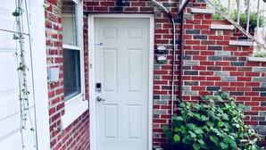 A white door with a small window above it, a red brick wall, and a green plant in front.