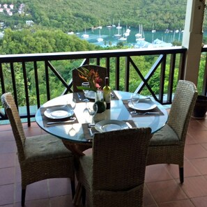 Une table pour deux, avec un plateau en verre, entourée de chaises en osier, donnant sur une marina remplie de bateaux.