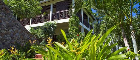 A two-story building with a balcony, surrounded by lush tropical vegetation.