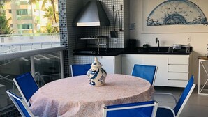 A modern kitchen with a tiled backsplash, a built-in oven, and a dining area with a round table and blue chairs. - Renovated building, 170m2, 4 bedrooms - air conditioning, terrace and barbecue, beachfront. (Bertioga)