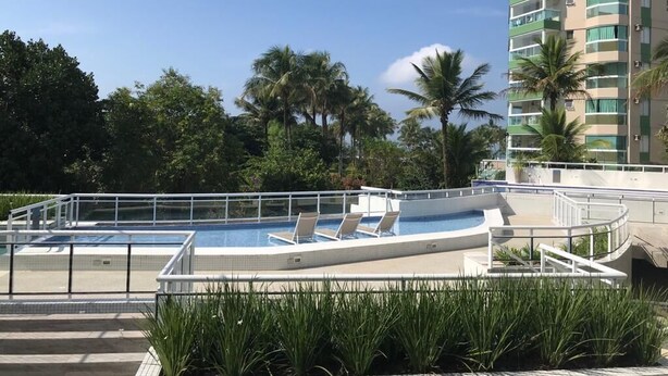 A swimming pool with lounge chairs, surrounded by a white fence, and palm trees in the background. - Renovated building, 170m2, 4 bedrooms - air conditioning, terrace and barbecue, beachfront. (Bertioga)
