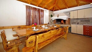 A wooden dining table set for six with benches, a stone fireplace, and a kitchen area with cabinets.
