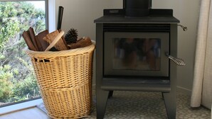 A room with a black wood-burning stove, a wicker basket with items, and a window with a view of trees.