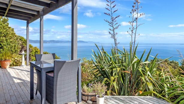 An outdoor deck with a table and chairs, surrounded by potted plants and overlooking a scenic view of the ocean.