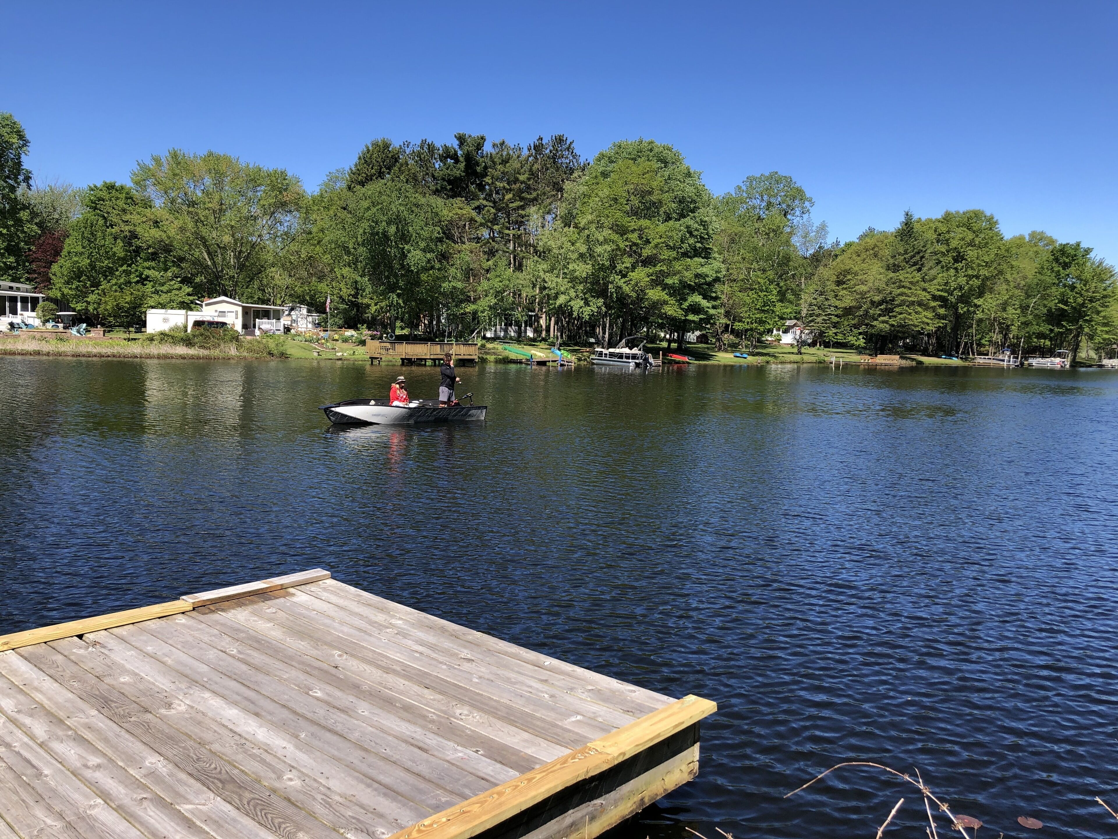 A wooden dock extending into a calm lake with a small boat and a person on it.