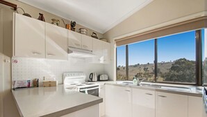 A modern kitchen with white cabinets, a built-in oven, and a large window offering a view of the countryside. - Elm Cottage Tumut -Blue Gum a Pet Friendly cosy 2 bedroom Cottage -  river views (Tumut)