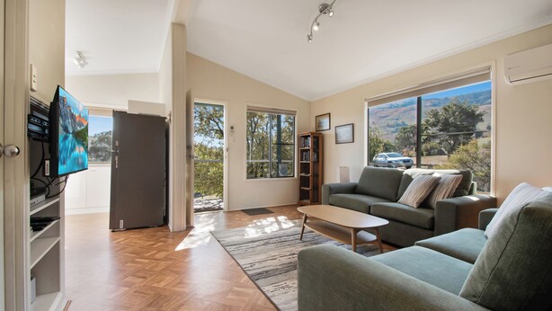 A spacious living room with a large window, a sofa, a coffee table, and a TV. - Elm Cottage Tumut -Blue Gum a Pet Friendly cosy 2 bedroom Cottage -  river views (Tumut)
