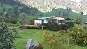 A house with a green roof and white walls, surrounded by lush greenery and hills. - Elm Cottage Tumut -Blue Gum a Pet Friendly cosy 2 bedroom Cottage -  river views (Tumut)
