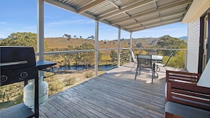 A covered outdoor deck with a grill, seating, and a view of rolling hills. - Elm Cottage Tumut -Blue Gum a Pet Friendly cosy 2 bedroom Cottage -  river views (Tumut)