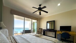 Habitación de hotel con cama, escritorio con televisor, silla y balcón con vista al mar.