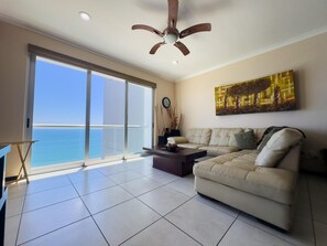 A living room with a large sliding glass door leading to a balcony, a ceiling fan, a beige sofa, and a painting on the wall.